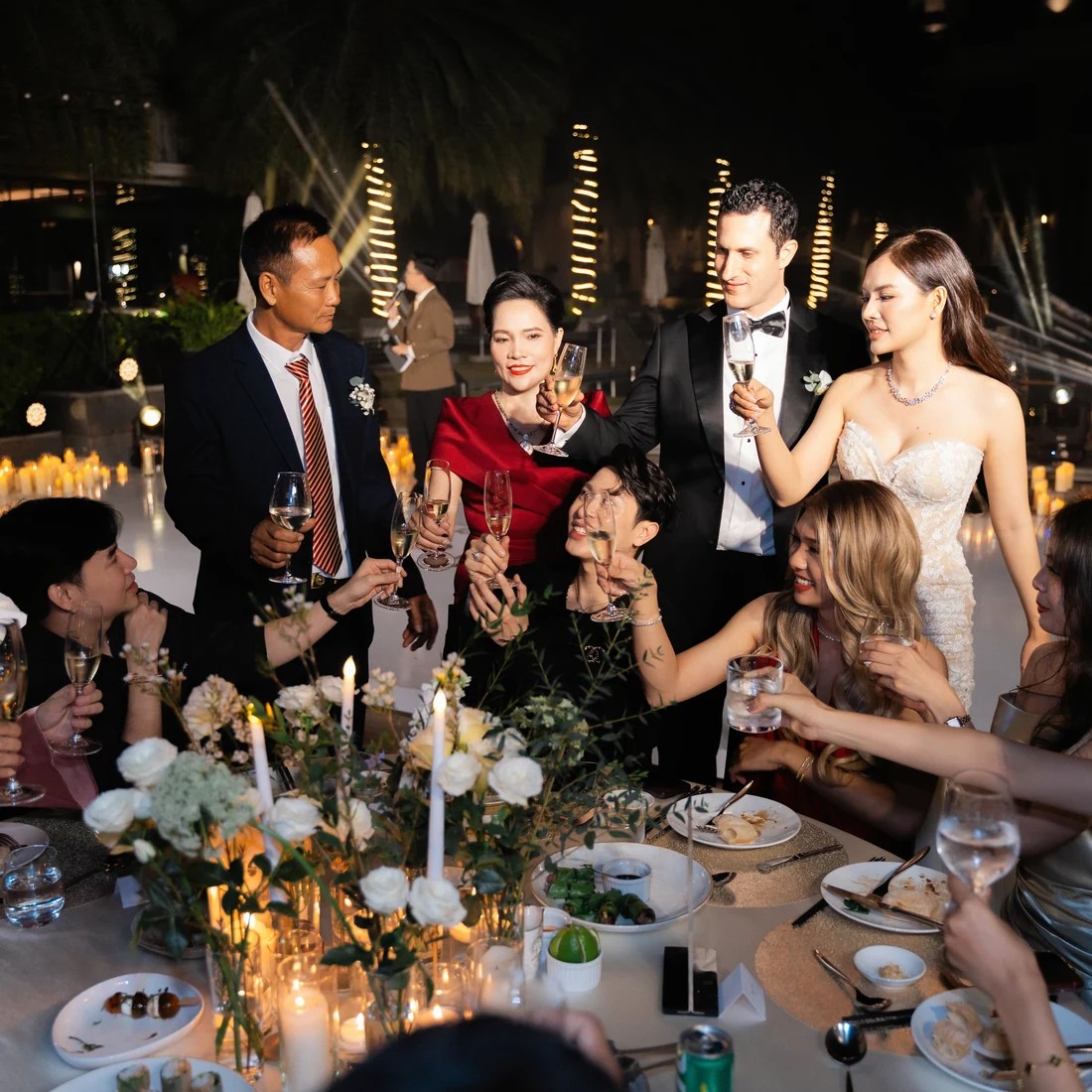 Bride and groom toasting with guests during an evening wedding dinner